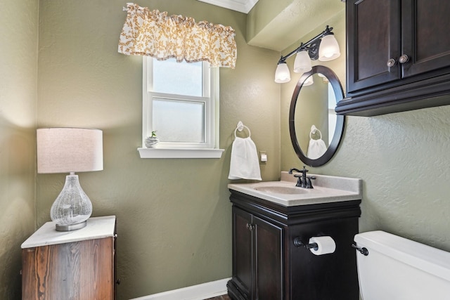 half bathroom featuring toilet, a textured wall, vanity, and baseboards