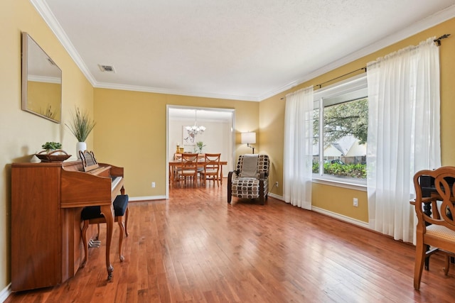 sitting room featuring visible vents, hardwood / wood-style floors, ornamental molding, a chandelier, and baseboards