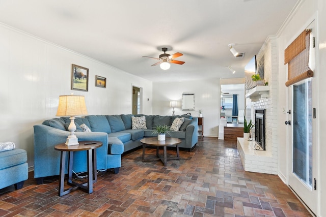 living room with brick floor, a fireplace, ornamental molding, and a ceiling fan