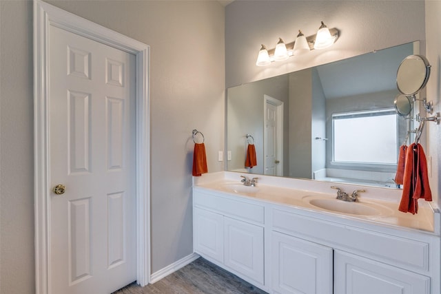 full bath with double vanity, wood finished floors, a sink, and baseboards