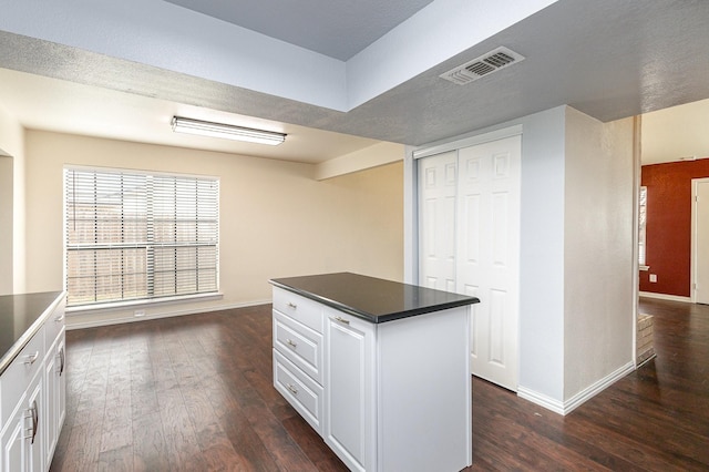 kitchen with dark wood-type flooring, a kitchen island, visible vents, white cabinetry, and dark countertops