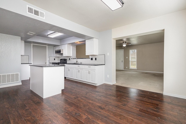 kitchen with stainless steel microwave, dark countertops, a sink, and visible vents