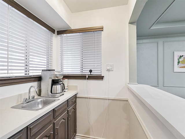 kitchen featuring a wainscoted wall, light countertops, a decorative wall, a sink, and dark brown cabinetry