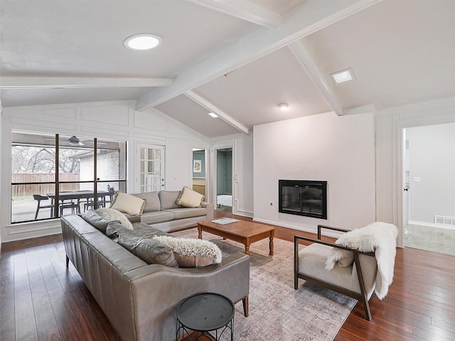 living room with vaulted ceiling with beams, hardwood / wood-style flooring, a glass covered fireplace, and visible vents