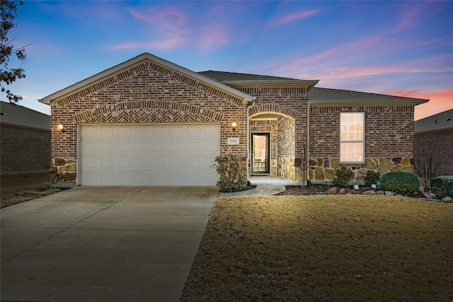 view of front of house featuring roof with shingles, an attached garage, concrete driveway, stone siding, and brick siding