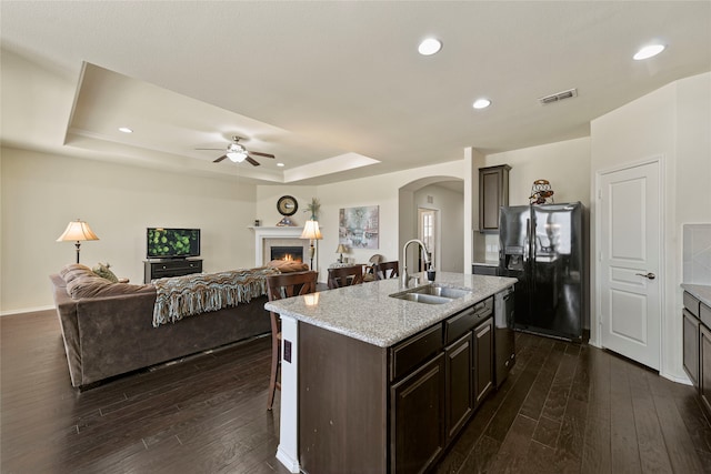 kitchen featuring visible vents, a lit fireplace, a tray ceiling, black fridge with ice dispenser, and a sink