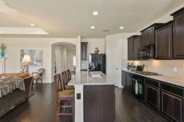 kitchen with visible vents, a sink, arched walkways, black appliances, and dark wood-style flooring