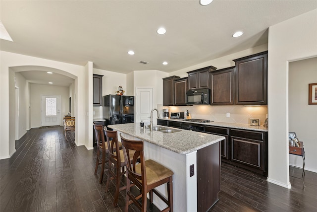 kitchen featuring black appliances, a breakfast bar, a sink, dark wood-style floors, and arched walkways