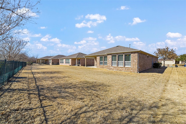 rear view of house with a yard, brick siding, and fence