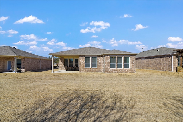 rear view of house featuring a patio, a lawn, brick siding, and a shingled roof