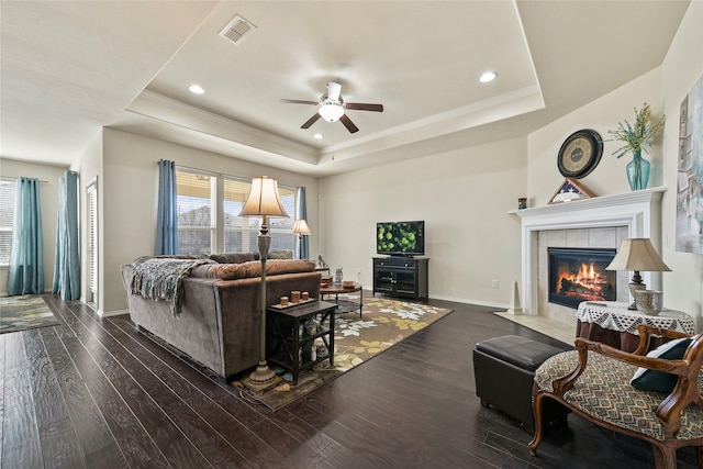 living room with visible vents, dark wood-type flooring, baseboards, a tiled fireplace, and a tray ceiling