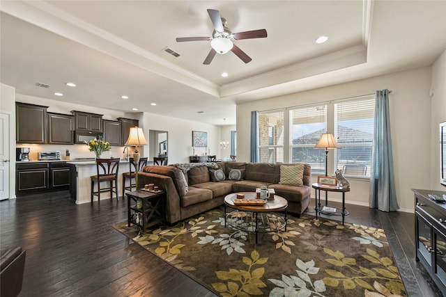 living area with dark wood finished floors, a raised ceiling, visible vents, and ornamental molding