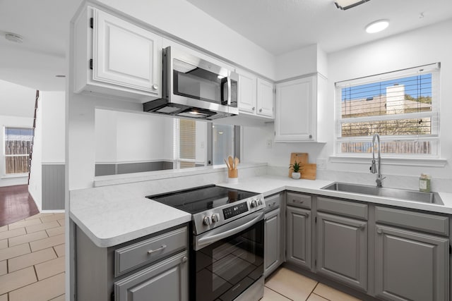 kitchen featuring white cabinets, appliances with stainless steel finishes, light countertops, gray cabinetry, and a sink