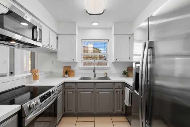 kitchen featuring light countertops, stainless steel appliances, gray cabinetry, a sink, and light tile patterned flooring