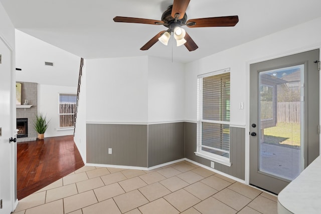 interior space featuring ceiling fan, tile patterned flooring, visible vents, wainscoting, and a brick fireplace