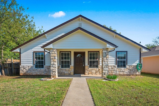 view of front of home with covered porch, stone siding, fence, and a front lawn