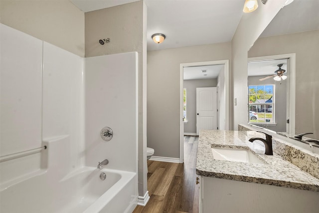 bathroom with toilet, vanity, shower / tub combination, wood finished floors, and baseboards