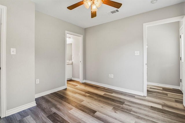 unfurnished bedroom with wood finished floors, a ceiling fan, visible vents, baseboards, and ensuite bath