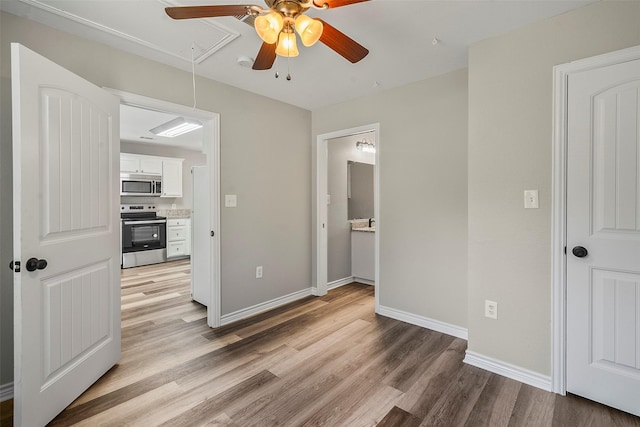 bedroom with ceiling fan, baseboards, light wood-style floors, ensuite bath, and attic access