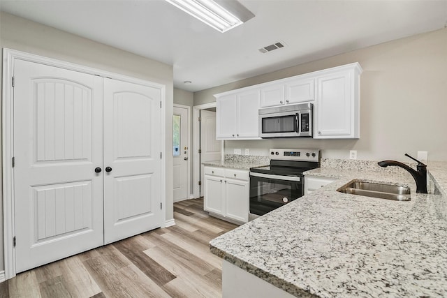 kitchen with white cabinets, light stone countertops, stainless steel appliances, and a sink