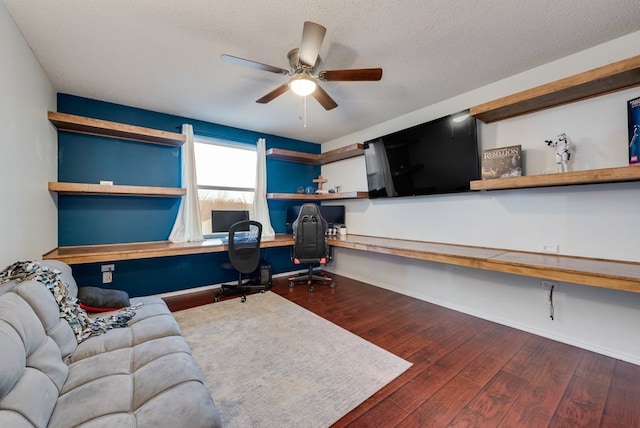 office area featuring baseboards, ceiling fan, dark wood-style flooring, a textured ceiling, and built in desk