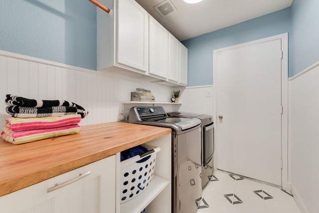 washroom with cabinet space, visible vents, washer and dryer, and a wainscoted wall