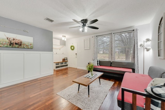 living room with a ceiling fan, visible vents, a textured ceiling, and wood finished floors