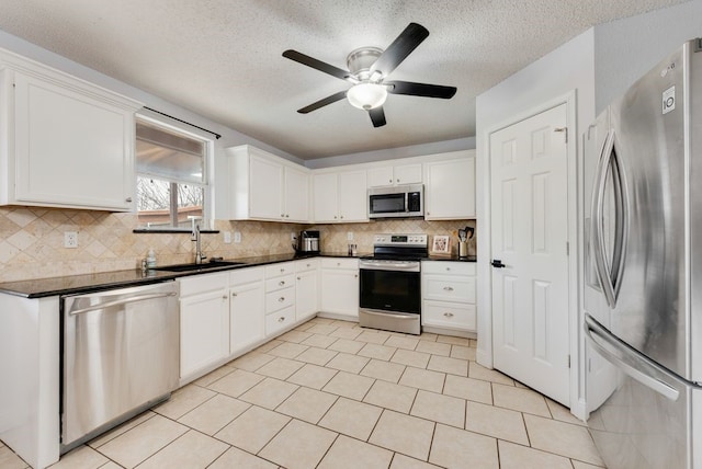 kitchen with stainless steel appliances, dark countertops, decorative backsplash, white cabinets, and a sink