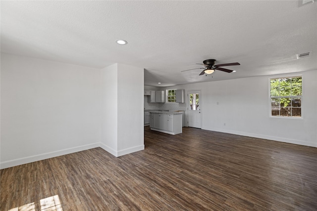 unfurnished living room featuring dark wood-style flooring, visible vents, plenty of natural light, and baseboards