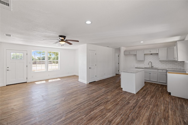 kitchen featuring a center island, visible vents, backsplash, dark wood-type flooring, and a sink