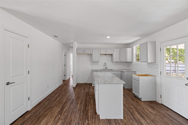 kitchen with a sink, baseboards, backsplash, a center island, and dark wood finished floors