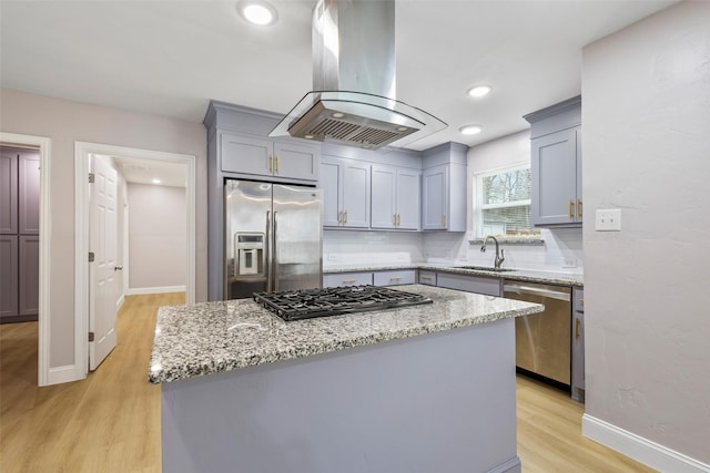 kitchen featuring island exhaust hood, light wood finished floors, stainless steel appliances, gray cabinetry, and a sink