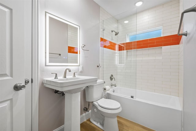 bathroom featuring baseboards, toilet, wood finished floors, washtub / shower combination, and a sink