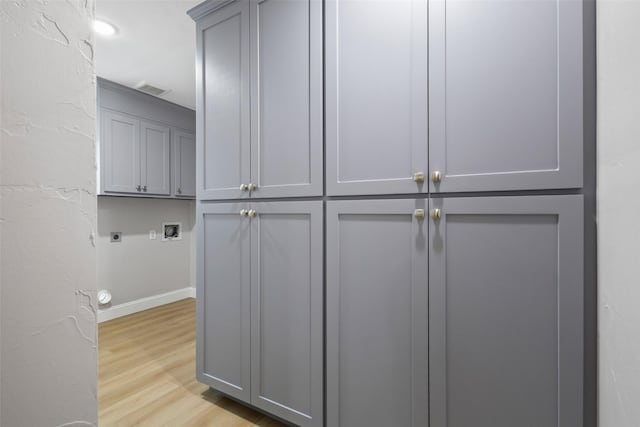 laundry area featuring light wood finished floors, hookup for a washing machine, cabinet space, hookup for an electric dryer, and baseboards