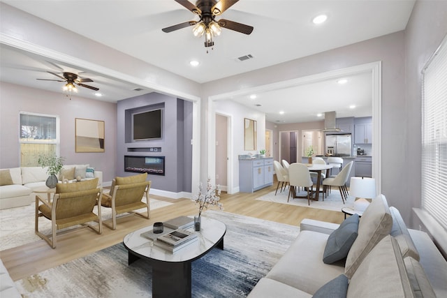 living area featuring light wood-type flooring, a glass covered fireplace, visible vents, and recessed lighting