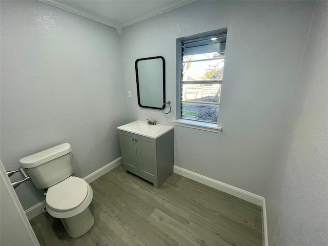 half bathroom with wood finished floors, ornamental molding, toilet, vanity, and baseboards