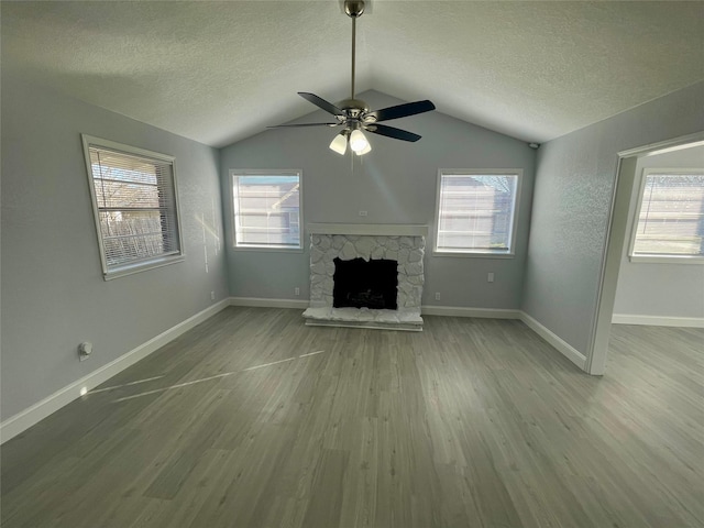 unfurnished living room featuring a ceiling fan, a stone fireplace, a textured ceiling, wood finished floors, and lofted ceiling