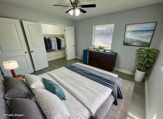 bedroom with a closet, a spacious closet, ceiling fan, wood finished floors, and baseboards