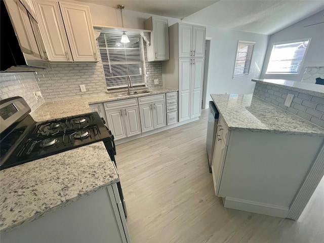 kitchen featuring lofted ceiling, light stone counters, stainless steel appliances, light wood-type flooring, and a sink