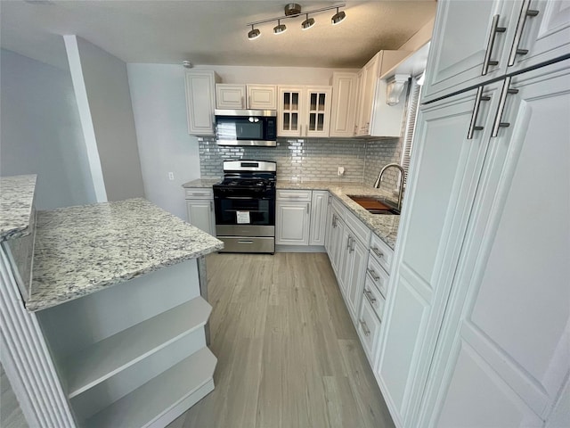 kitchen featuring stainless steel appliances, a sink, tasteful backsplash, light wood finished floors, and white cabinetry