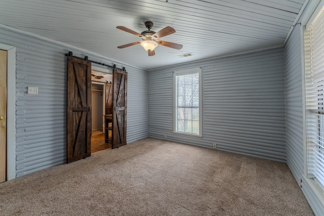 unfurnished bedroom with carpet, crown molding, visible vents, a barn door, and a ceiling fan