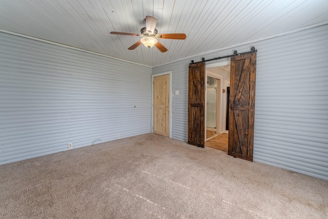 unfurnished bedroom featuring a barn door, ceiling fan, and carpet flooring