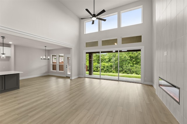 unfurnished living room with baseboards, plenty of natural light, a towering ceiling, and ceiling fan with notable chandelier