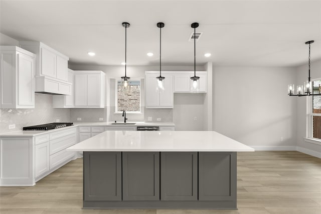 kitchen featuring visible vents, baseboards, white cabinets, a sink, and gas stovetop