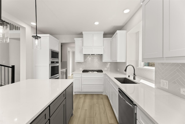 kitchen featuring hanging light fixtures, a sink, appliances with stainless steel finishes, white cabinetry, and light wood-style flooring