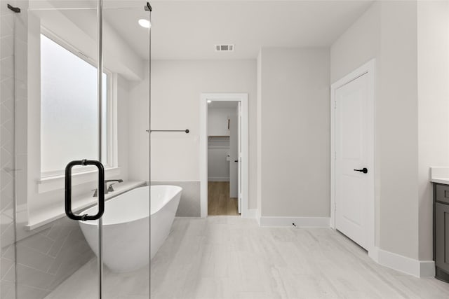 bathroom with a freestanding bath, vanity, baseboards, and a spacious closet