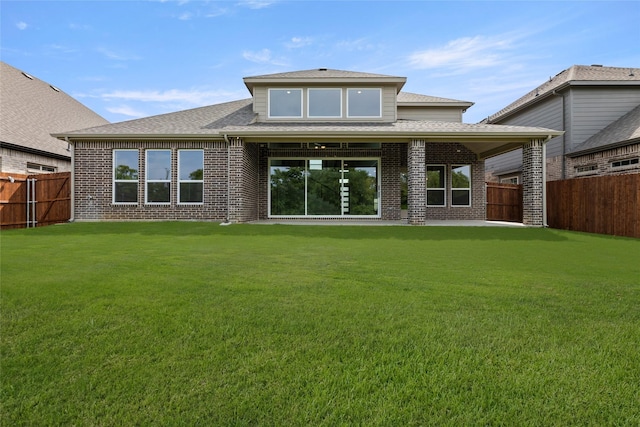rear view of property with roof with shingles, a yard, brick siding, and a fenced backyard