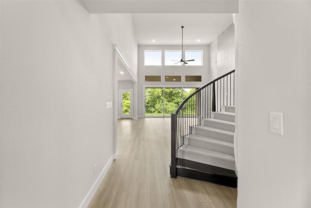 staircase with baseboards, a ceiling fan, recessed lighting, a towering ceiling, and wood finished floors