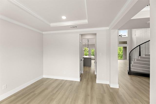 spare room with ornamental molding, stairs, visible vents, a tray ceiling, and light wood finished floors