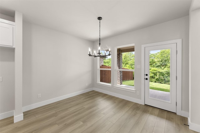 unfurnished dining area with a chandelier, light wood-type flooring, and baseboards